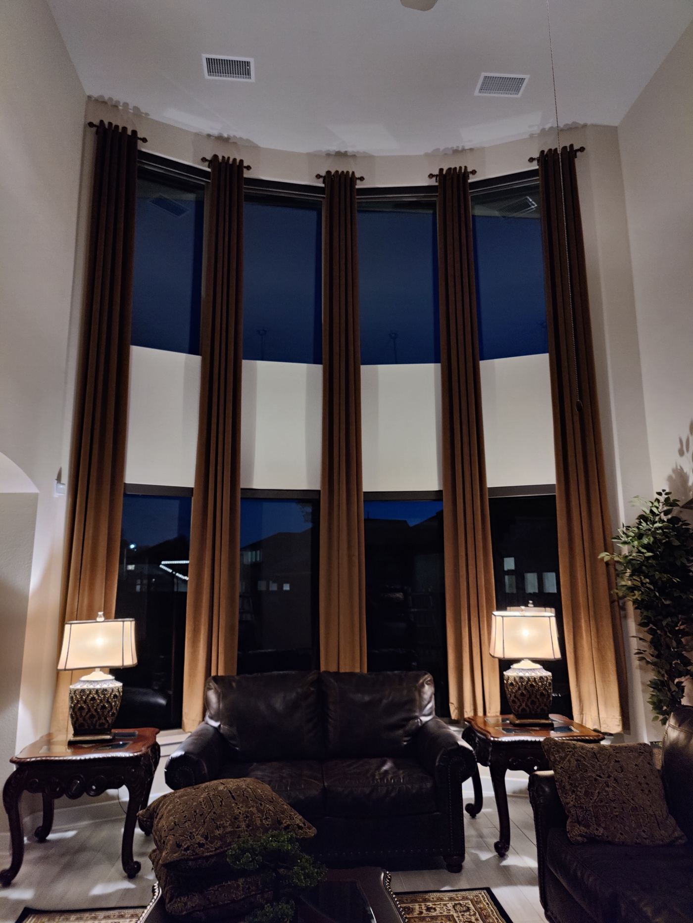 Long curtain panels on decorative rods above a curved two-tier window wall