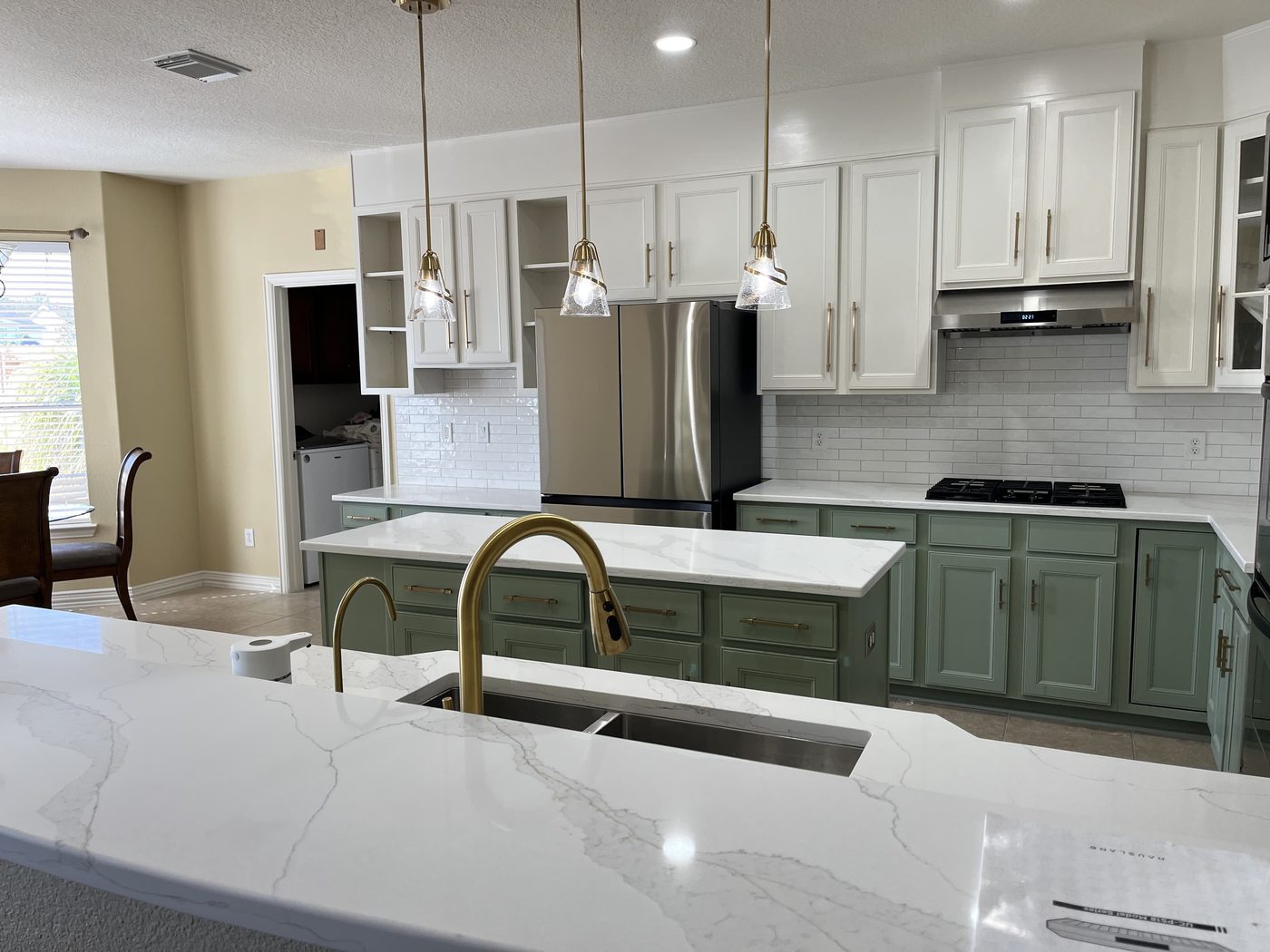 Finished two-tone kitchen with a sage green island, white upper cabinets, quartz counters, and gold fixtures