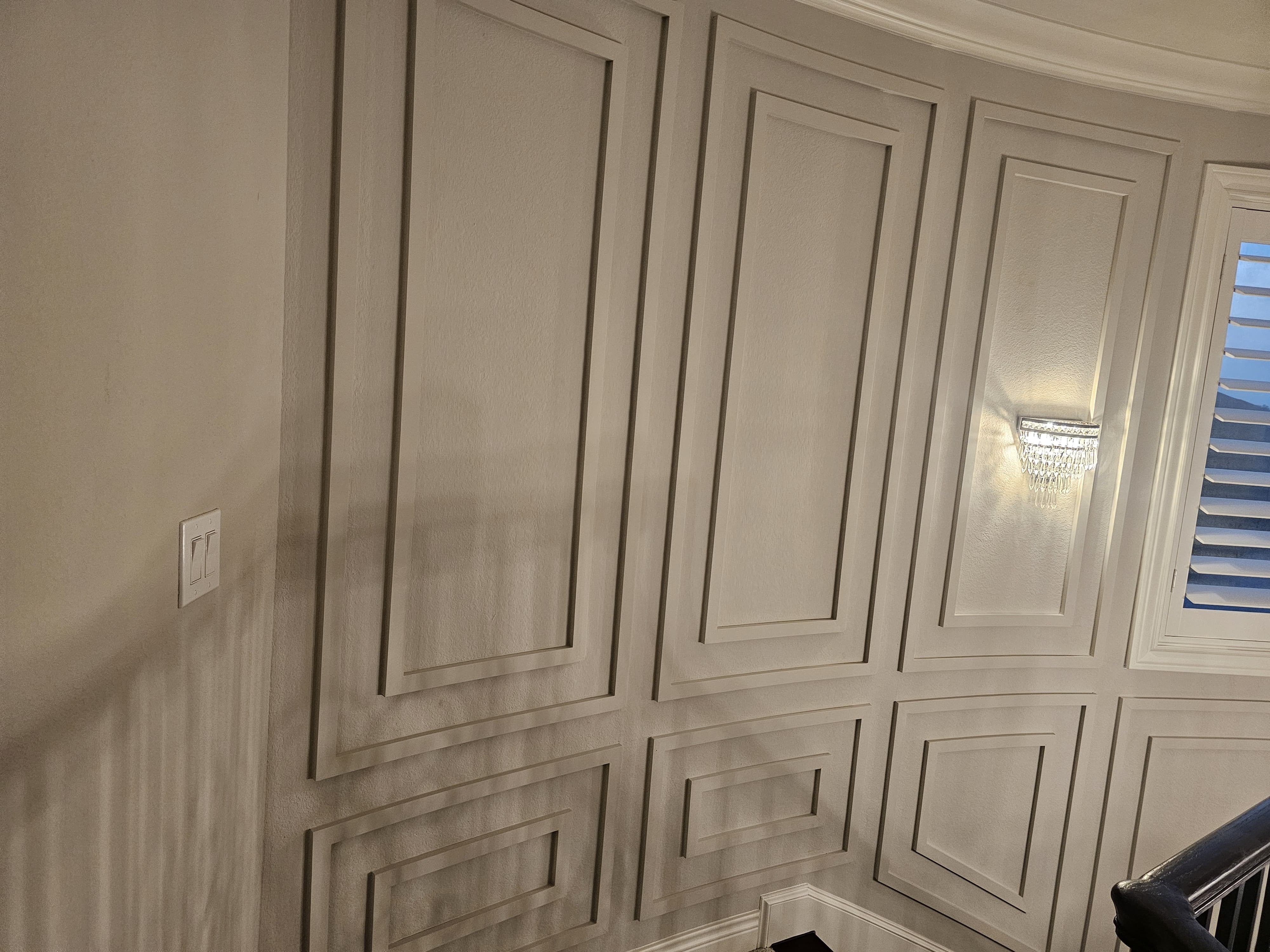 Curved stair wall with layered picture-frame molding and a lit crystal wall sconce.