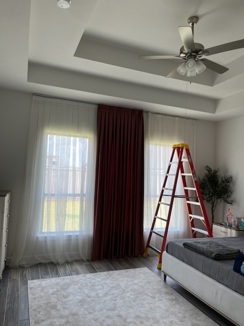 Bedroom with curtains on a long rod and a ladder positioned at the windows.