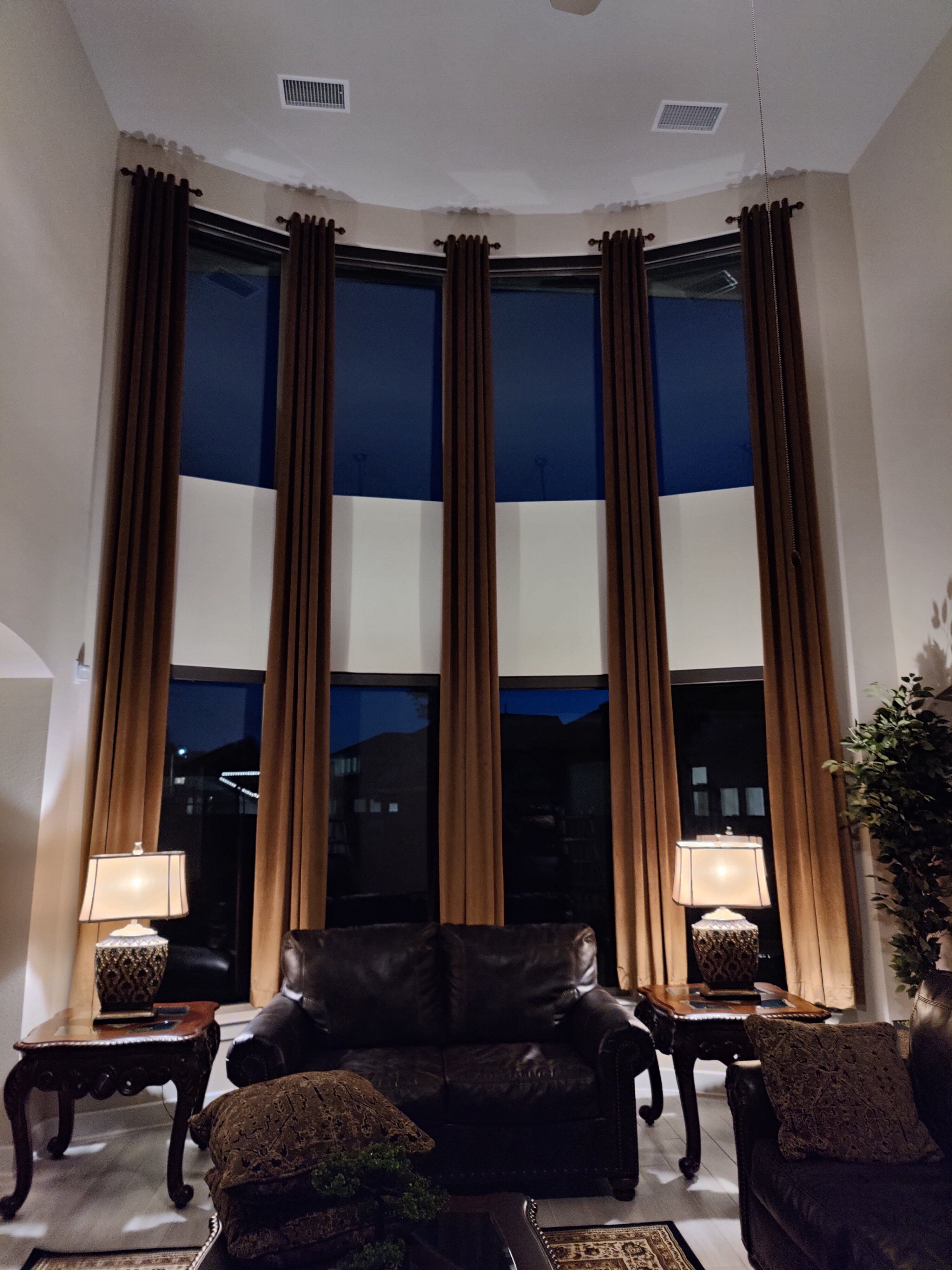 Tall living room with long curtain panels over a curved two-tier window wall.