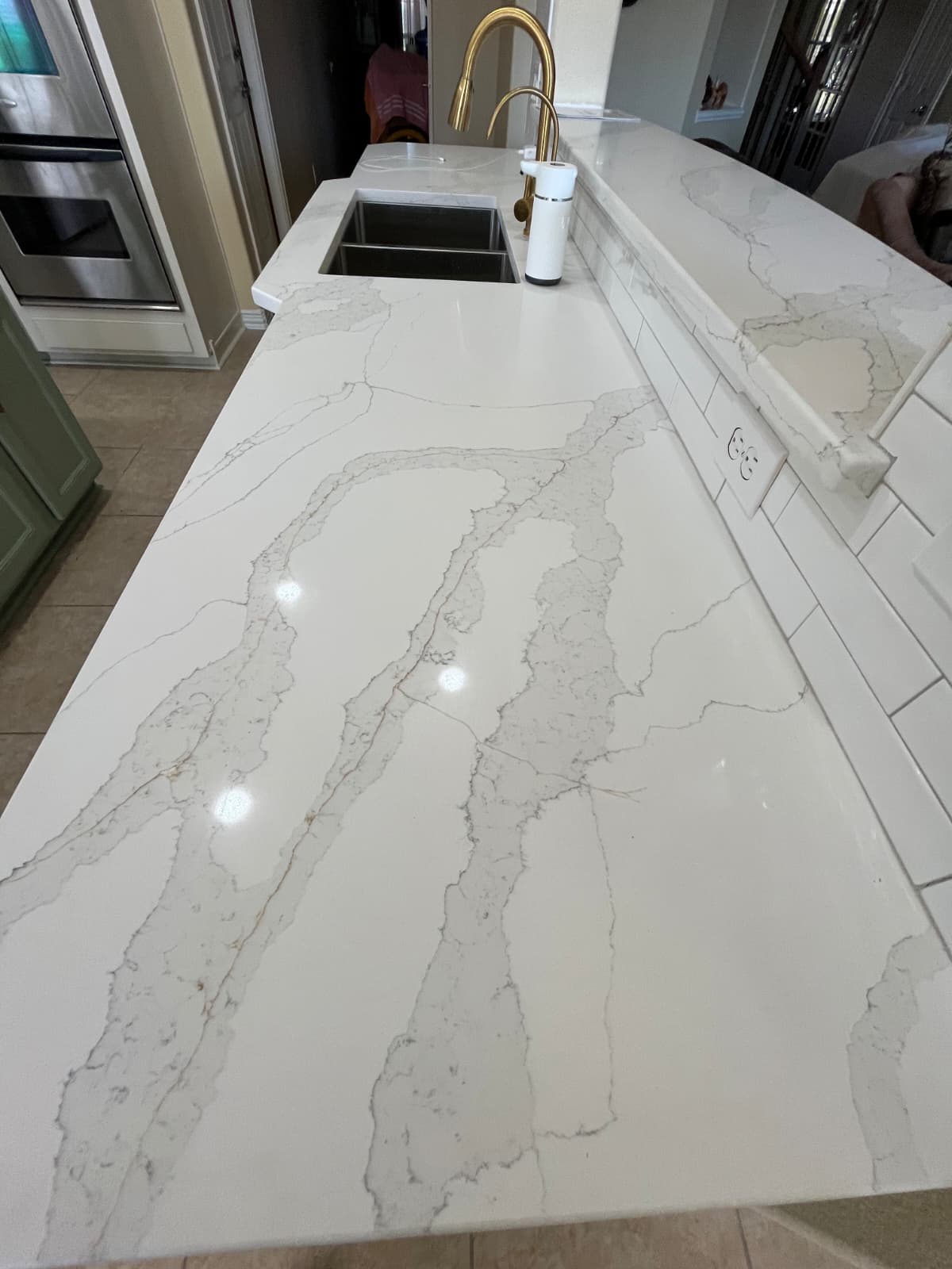White quartz kitchen countertop with gold faucet and white subway-tile backsplash.