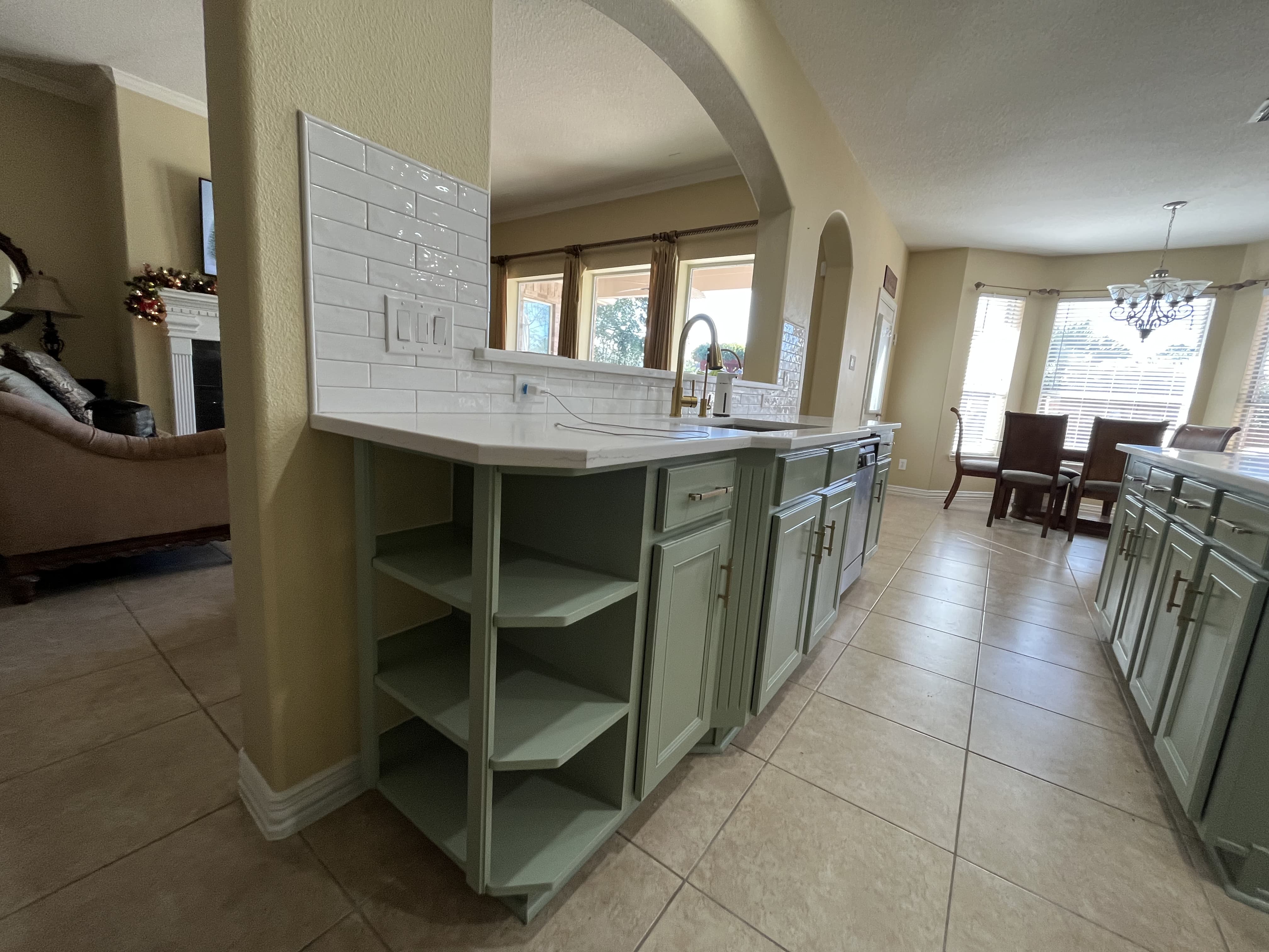 Sage green kitchen peninsula with subway tile backsplash and quartz countertop.