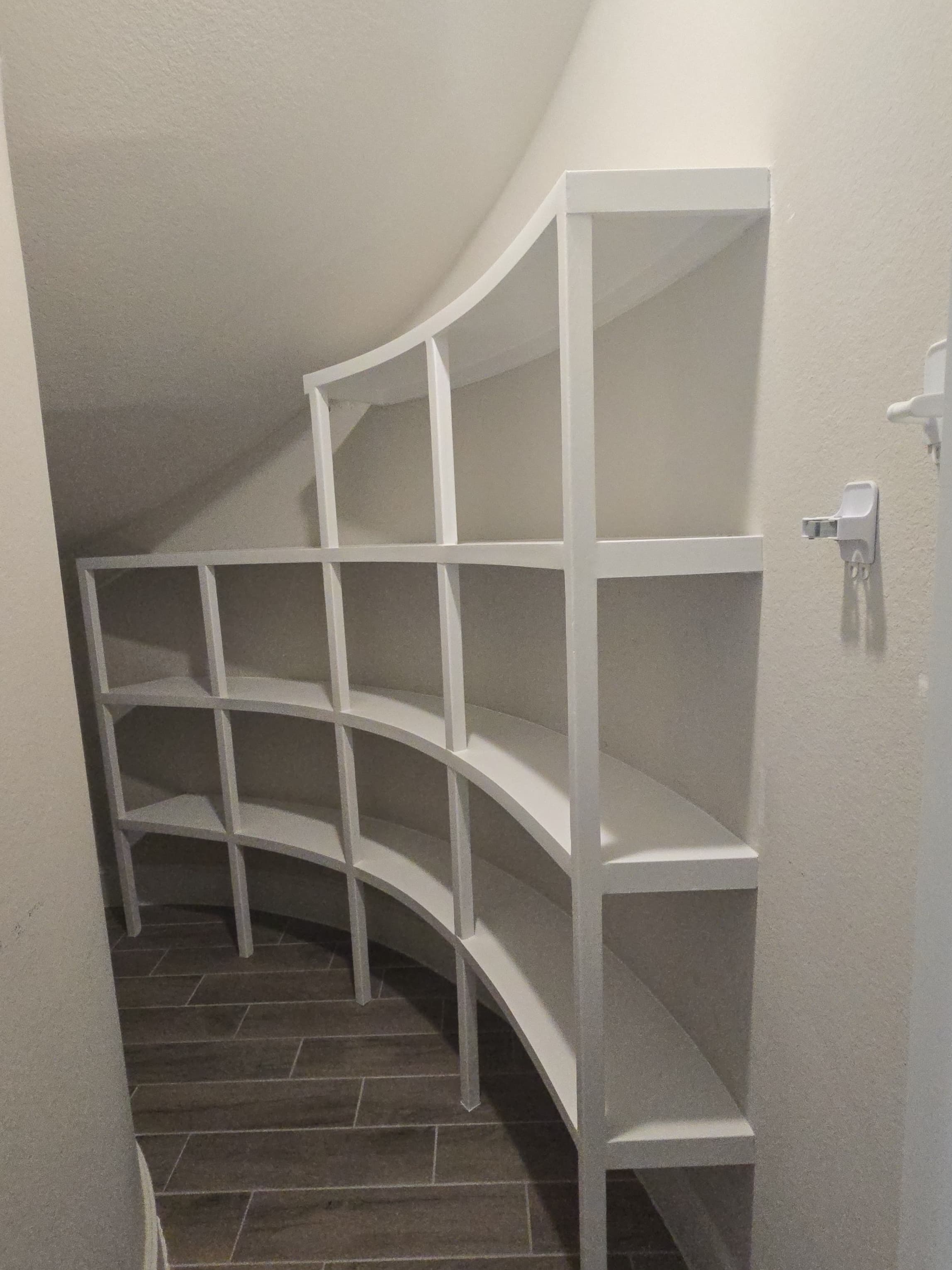 Custom white built-in shelves following a curved under-stairs space.