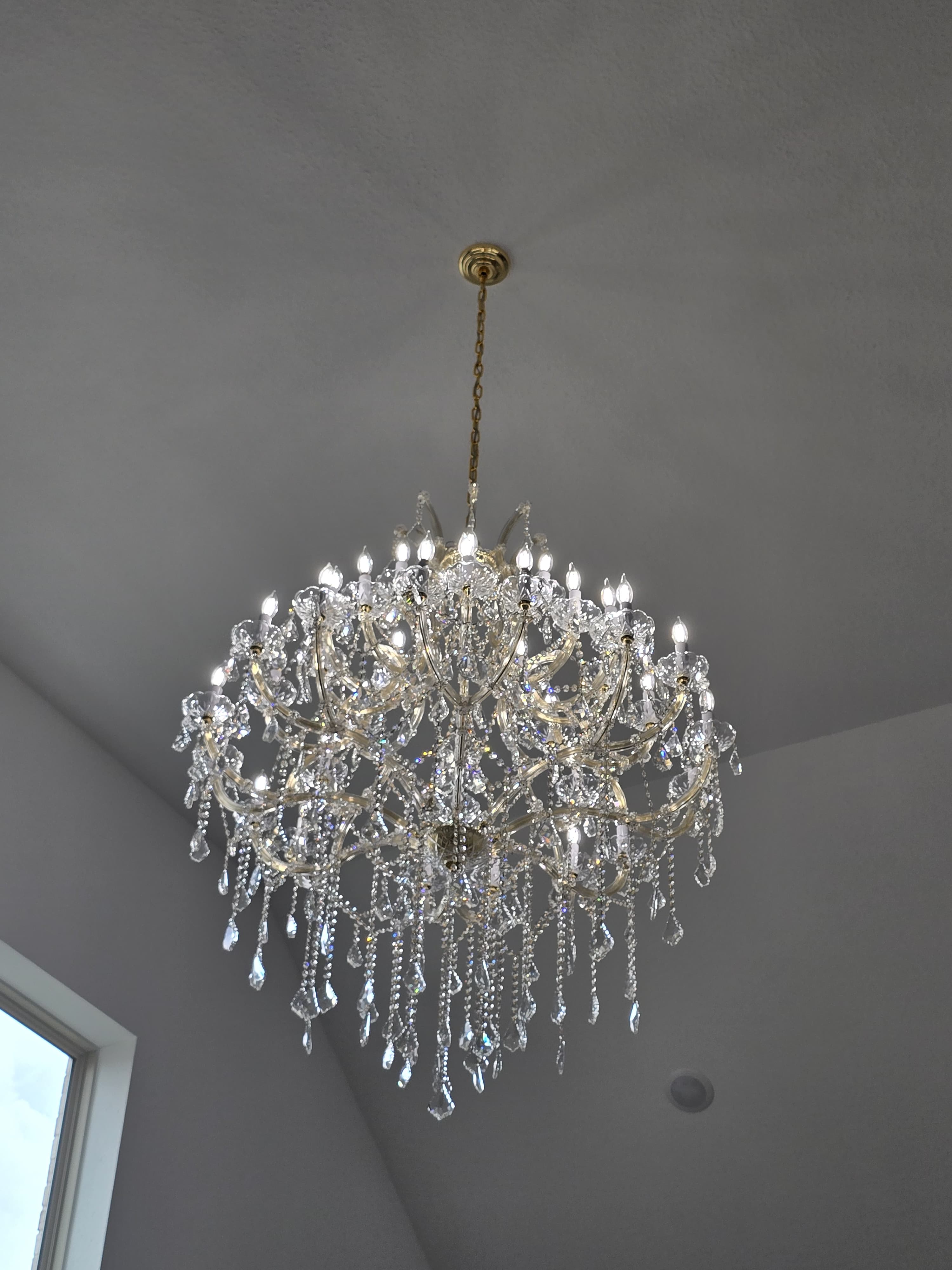 Looking up at an ornate gold and crystal chandelier with lit candle-style bulbs.