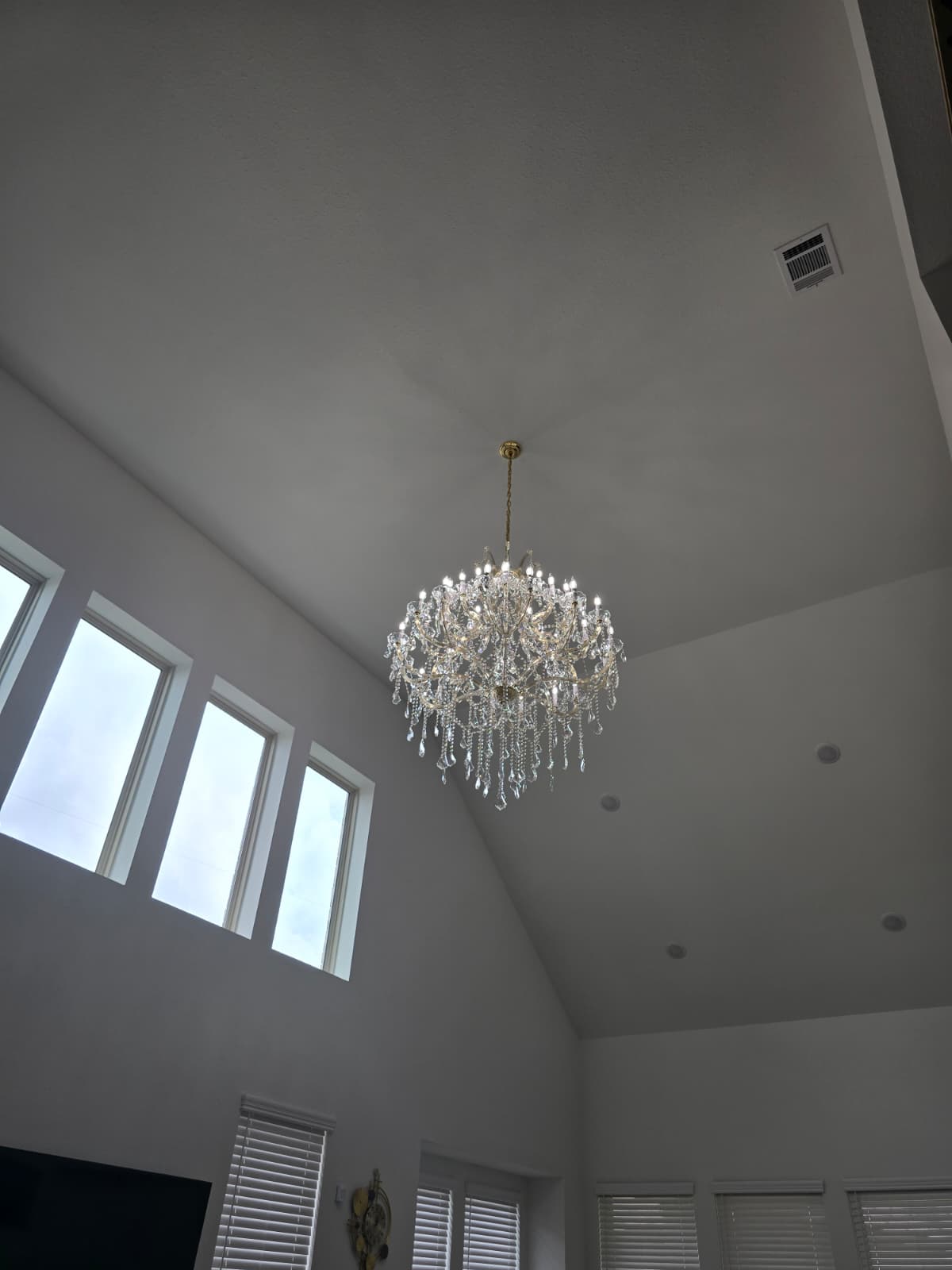 Large crystal chandelier hanging in a bright vaulted-ceiling living space.