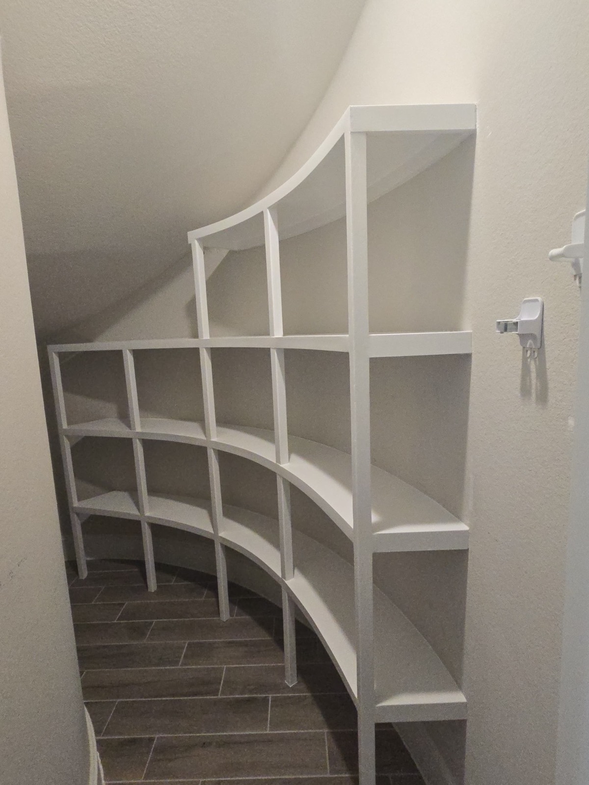 Custom white built-in shelves following a curved under-stairs space.