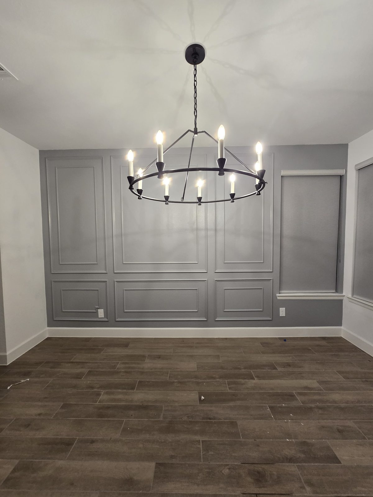Dining space with wood-look tile flooring, box-molding accent wall, and chandelier