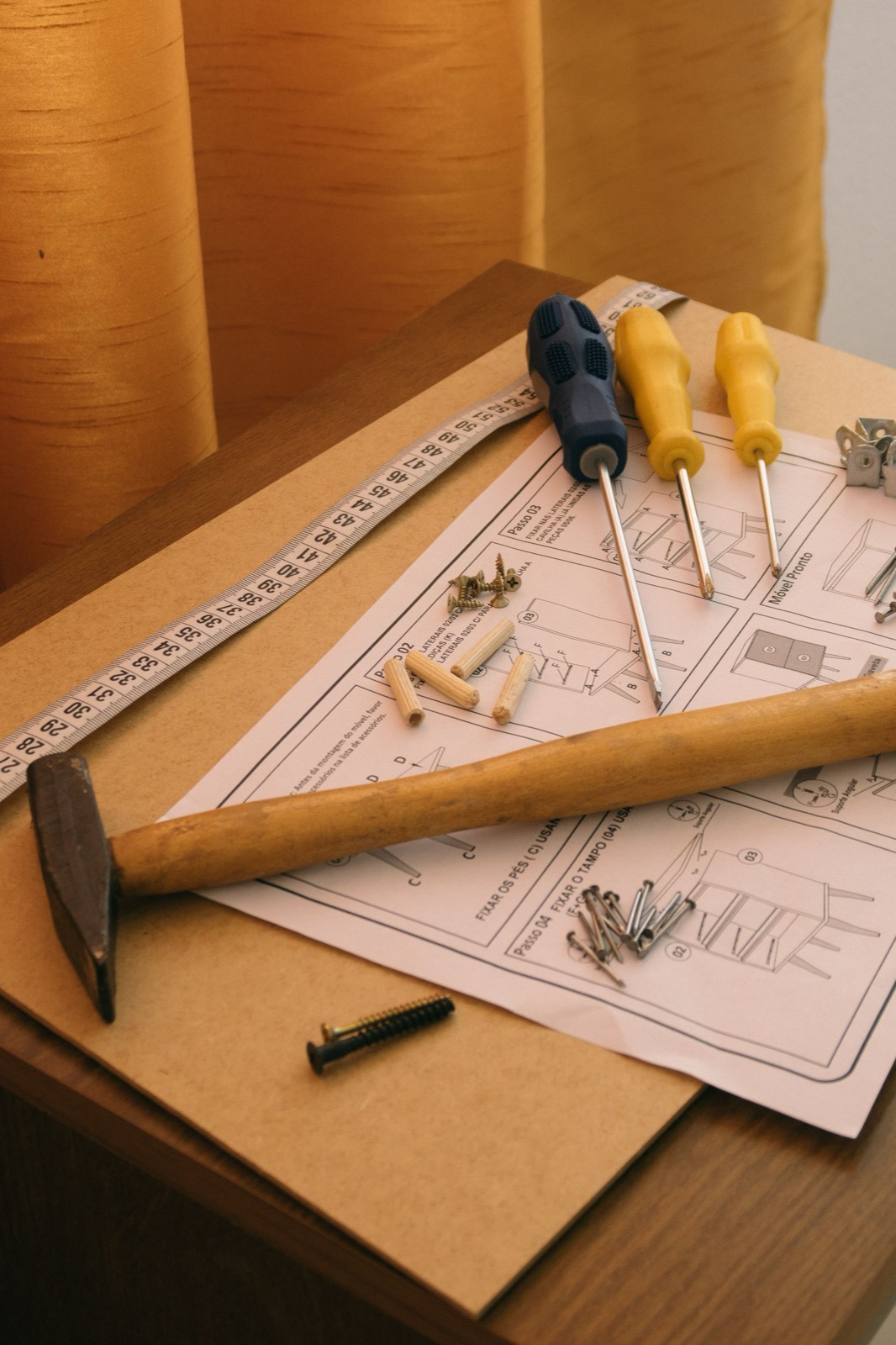 A hammer, screwdrivers, wooden dowels and screws resting on a printed furniture assembly instruction sheet
