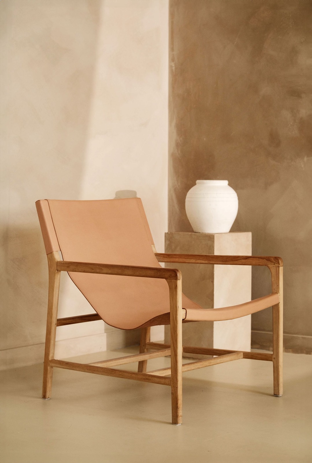 A room with warm limewashed plaster walls in cream and tan tones, with a wood-frame leather sling chair