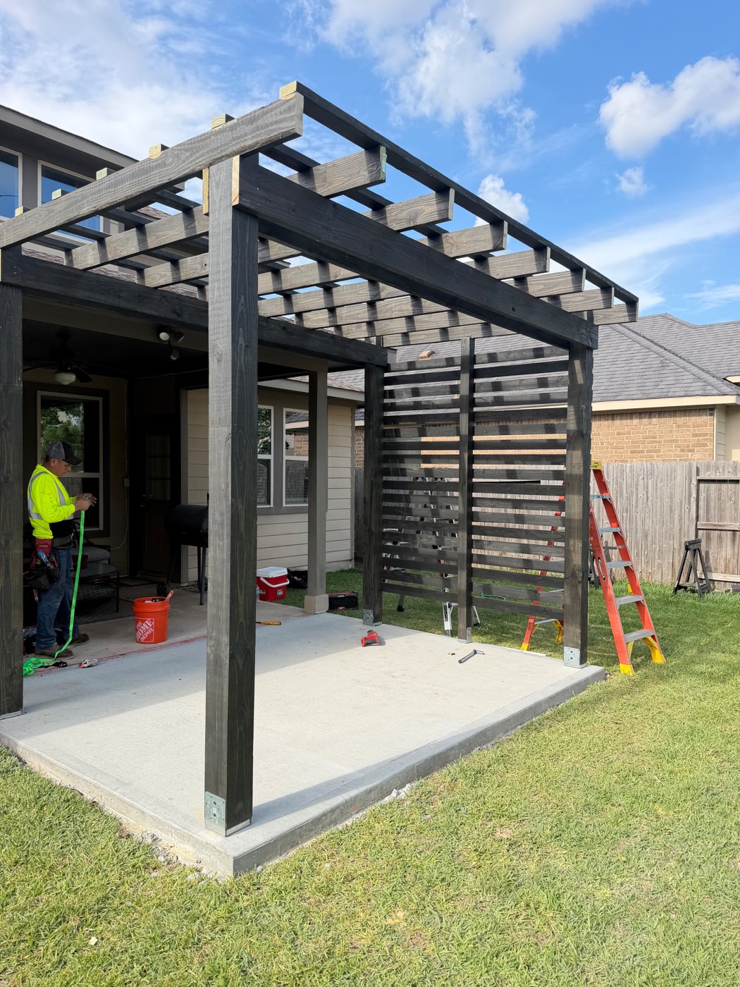 Dark-stained wood pergola and privacy-slat wall under construction on a West Houston concrete patio